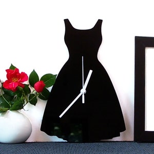 May include: Black silhouette of a dress with white clock hands. The clock is mounted on a white wall.
