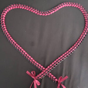 May include: A black and burgundy ribbon lei in the shape of a heart. The lei is tied with two bows at the ends.