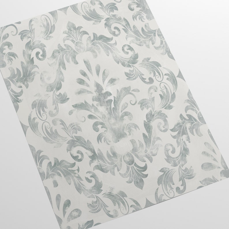 Puede incluir: Una hoja de papel pintado con un patr&oacute;n de damasco cl&aacute;sico. El dise&ntilde;o presenta elementos florales estilizados y ondulados en un color verde azulado apagado sobre un fondo blanco. El patr&oacute;n est&aacute; distribuido uniformemente.