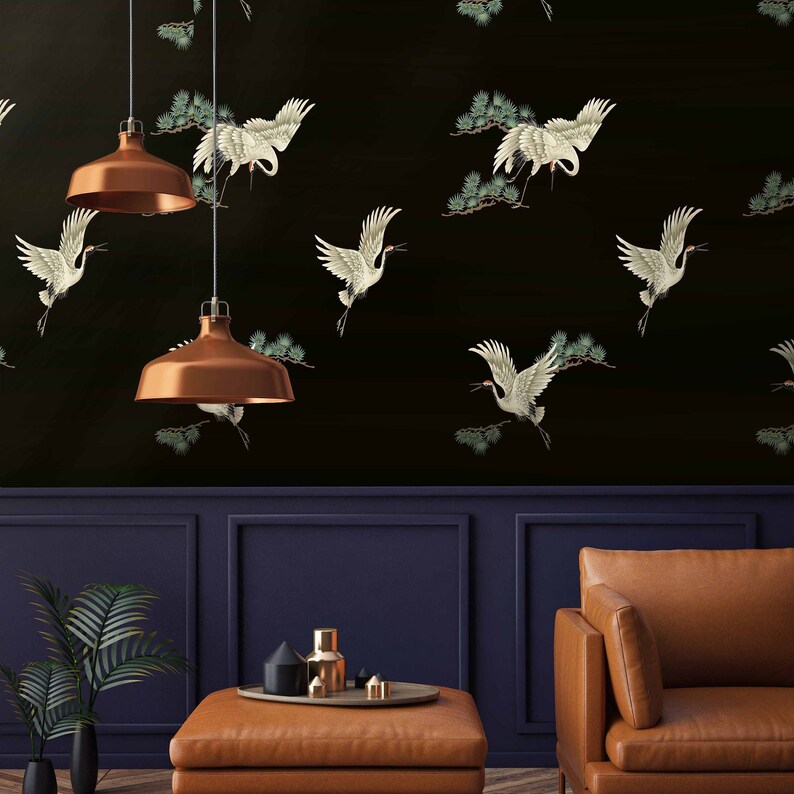 May include: A black and white wallpaper with a repeating pattern of white cranes flying against a black background. The wallpaper is in a room with a brown leather couch and a coffee table with a tray of decorative objects.