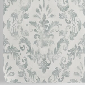 Puede incluir: Primer plano de una muestra de papel pintado con un patr&oacute;n de damasco repetido. El dise&ntilde;o presenta un motivo floral azul gris&aacute;ceo claro sobre un fondo blanco. El patr&oacute;n tiene un aspecto desgastado y texturizado, con una ligera curvatura en el borde.