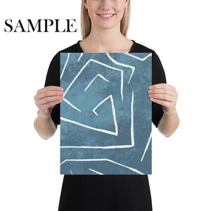 Puede incluir: Una impresi&oacute;n art&iacute;stica rectangular con un fondo verde azulado y l&iacute;neas geom&eacute;tricas blancas. La palabra "SAMPLE" est&aacute; impresa en negro en la parte superior. La impresi&oacute;n es sostenida por una persona.