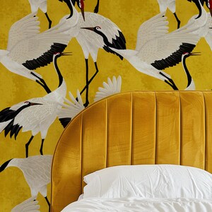 May include: A mustard yellow headboard with vertical channel tufting is paired with a white pillow and bedding. The background features a repeating pattern of white and black cranes on a yellow background.