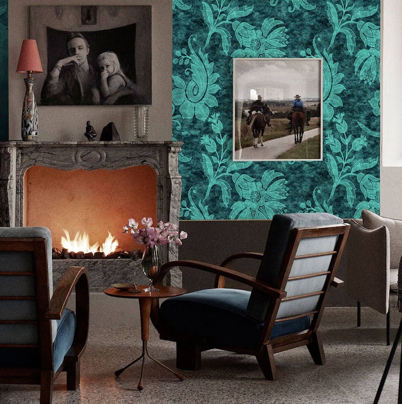 Pode incluir: Um papel de parede floral azul turquesa com uma foto emoldurada de duas pessoas a cavalo. O quarto tem uma lareira com fogo, duas poltronas e uma mesa pequena com um vaso de flores.