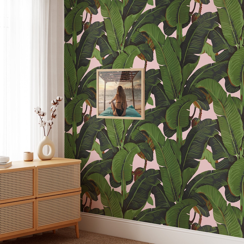 May include: A pink and green tropical banana leaf wallpaper with a framed photo of a person sitting on a beach.