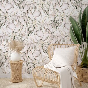 Puede incluir: Una silla de mimbre con una manta blanca y una almohada blanca se encuentra frente a una pared con un patr&oacute;n abstracto rosa y verde. Una peque&ntilde;a mesa auxiliar de mimbre con un jarr&oacute;n blanco y una planta frondosa se encuentra junto a la silla.