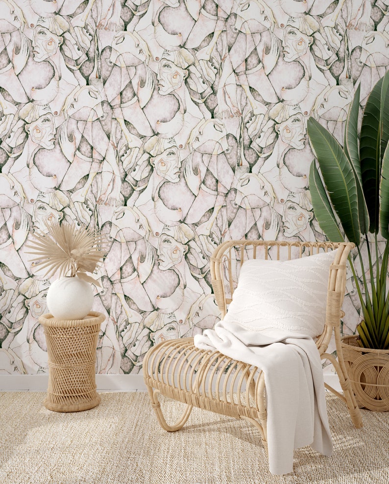 Puede incluir: Una silla de mimbre con una manta blanca y una almohada blanca se encuentra frente a una pared con un patr&oacute;n abstracto rosa y verde. Una peque&ntilde;a mesa auxiliar de mimbre con un jarr&oacute;n blanco y una planta frondosa se encuentra junto a la silla.