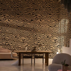 May include: A rectangular wooden dining table with four chairs, positioned against a wall covered in wallpaper featuring a black and beige wavy, organic line pattern. The room includes a curved beige sofa and a rounded white armchair in the foreground.