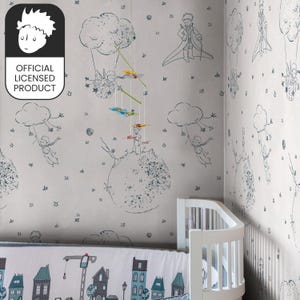 Può includere: Una cameretta con carta da parati con illustrazioni de Il Piccolo Principe, nuvole e stelle. Un mobile è appeso davanti al muro. La culla ha un paracolpi con una scena cittadina. L'immagine include il testo "OFFICIAL LICENSED PRODUCT".