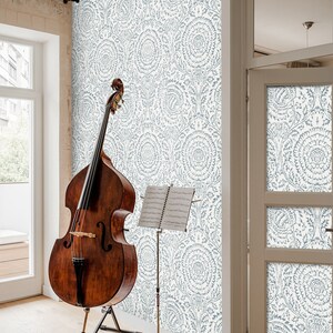 May include: A brown wooden double bass with a music stand holding sheet music in front of a wall with a blue and white floral pattern wallpaper.