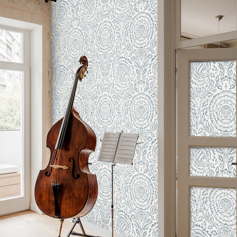 May include: A brown wooden double bass with a music stand holding sheet music in front of a wall with a blue and white floral pattern wallpaper.