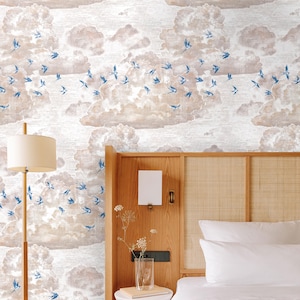 Pode incluir: Um quarto com uma cabeceira de madeira e uma cama com roupa de cama branca. A parede atr&aacute;s da cama &eacute; coberta com papel de parede com um padr&atilde;o de p&aacute;ssaros azuis voando sobre nuvens.