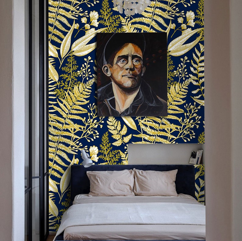 May include: A bedroom with a navy blue wall featuring a gold fern pattern wallpaper. A framed painting of a man wearing a black hat hangs above a bed with a white duvet and two beige pillows.