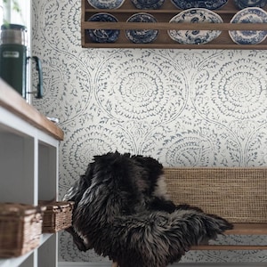 May include: A white and blue patterned wallpaper with a floral design. A bench with a sheepskin throw is in front of the wallpaper.