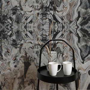May include: A black metal serving tray with two white ceramic mugs and a clear glass vase with a twig inside. The tray is sitting on a black metal stand with three legs. The background is a black and white abstract wallpaper with a swirling pattern.