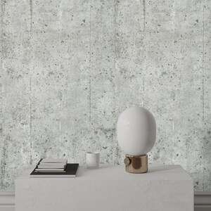 Puede incluir: Una l&aacute;mpara de mesa blanca con una pantalla redonda blanca y una base dorada se encuentra sobre una mesa blanca. Tambi&eacute;n hay una pila de libros y una taza blanca sobre la mesa. El fondo es una pared gris texturizada.