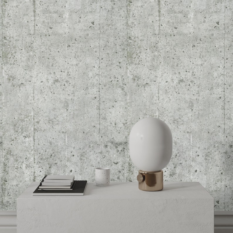 Puede incluir: Una l&aacute;mpara de mesa blanca con una pantalla redonda blanca y una base dorada se encuentra sobre una mesa blanca. Tambi&eacute;n hay una pila de libros y una taza blanca sobre la mesa. El fondo es una pared gris texturizada.