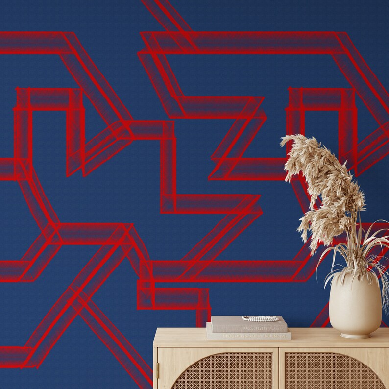 May include: A blue wall with a red geometric pattern. A wooden shelf with a book and a vase with dried flowers sits in front of the wall.