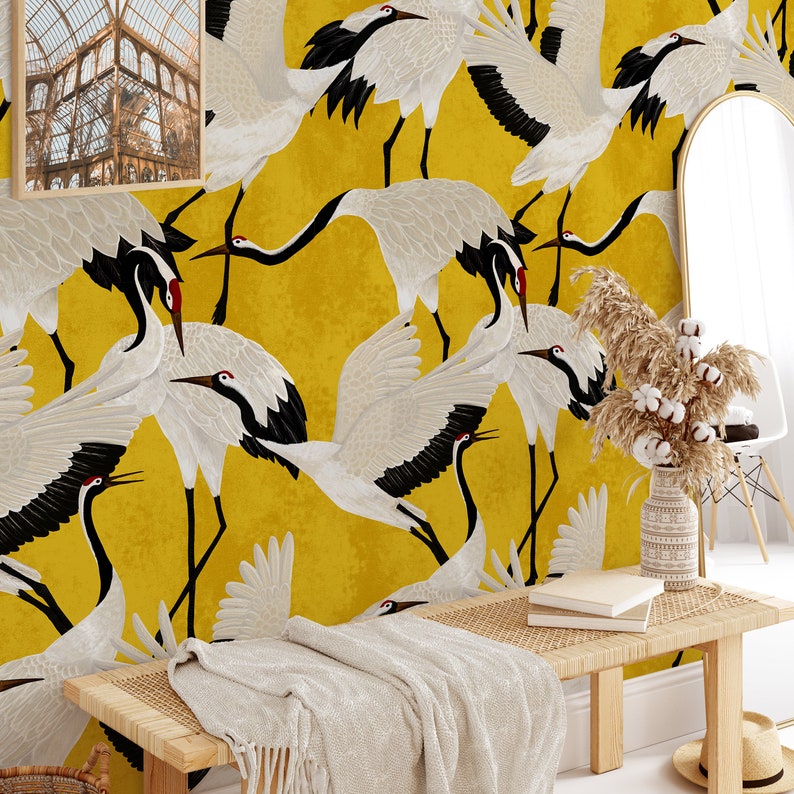 May include: A vibrant yellow wallpaper featuring a repeating pattern of white cranes with black wingtips and red accents. The birds are depicted in various poses against a textured background. The room is decorated with a bench, mirror, and framed artwork.