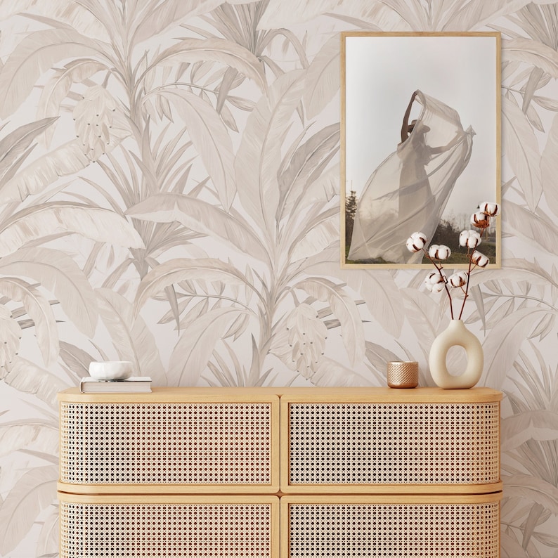Pu&ograve; includere: Una carta da parati marrone chiaro con un motivo a foglie tropicali. Un mobile in legno con una parte anteriore in rattan intrecciato &egrave; davanti alla carta da parati. Un quadro incorniciato di una donna con un vestito bianco &egrave; appeso al muro sopra il mobile. Un vaso con fiori di cotone &egrave; sul mobile.