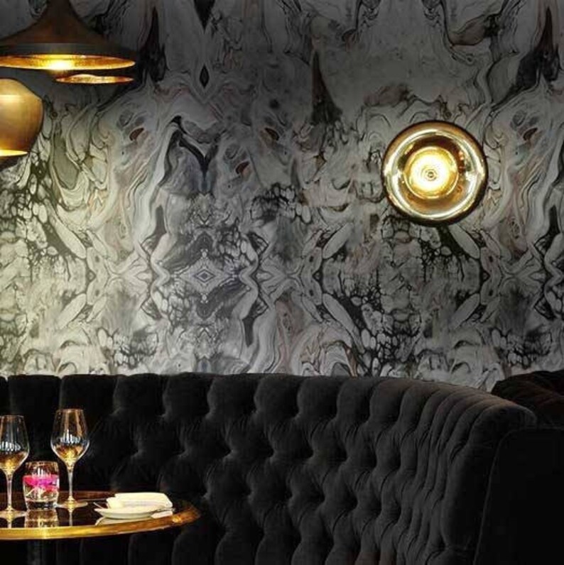 May include: A black tufted leather sofa with a gold-toned wall lamp and a marble-patterned wallpaper. The sofa is in a dining area with a round table and two wine glasses.