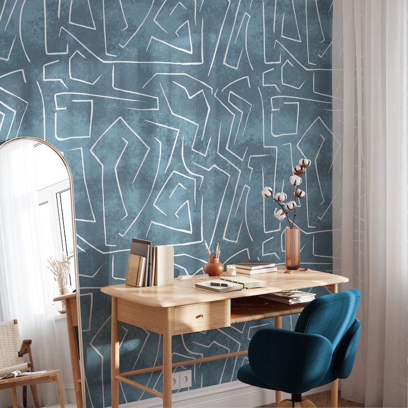 Puede incluir: Papel pintado azul turquesa con un dise&ntilde;o abstracto blanco. Un escritorio de madera con una silla turquesa, libros y un jarr&oacute;n con tallos de algod&oacute;n est&aacute;n frente al papel pintado. Un espejo y una silla est&aacute;n a la izquierda del escritorio.