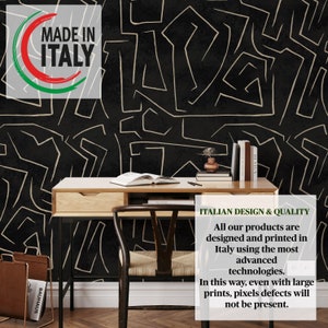 May include: Black and white abstract geometric pattern wallpaper with gold lines. The wallpaper is behind a wooden desk with a chair and books. The text "MADE IN ITALY" is in a red, white, and green circle in the upper left corner of the image. The text "ITALIAN DESIGN & QUALITY" is in the lower right corner of the image. The text below reads "All our products are designed and printed in Italy using the most advanced technologies. In this way, even with large prints, pixels defects will not be present."