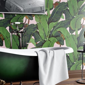 May include: A green freestanding bathtub with a white towel draped over the edge. The bathtub is in front of a wall covered in pink and green banana leaf wallpaper.