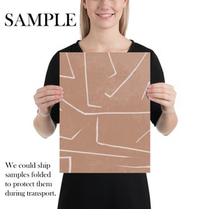 May include: A digital art print with an abstract design featuring white lines on a light brown background. The print is being held by a person.