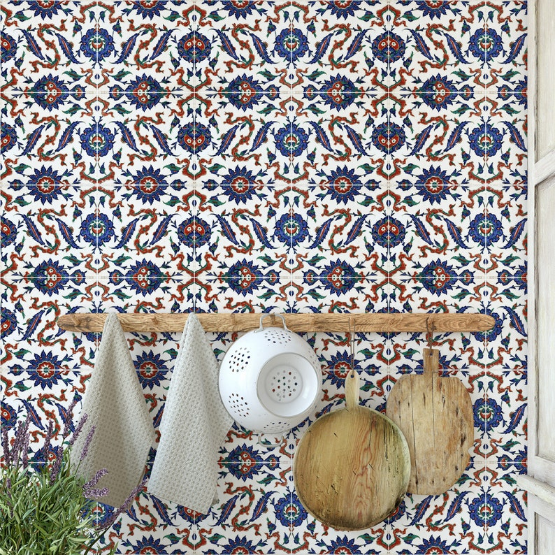 May include: A white tiled kitchen backsplash with a blue and red floral pattern. A wooden rack with two dish towels, a colander, and two wooden cutting boards hangs on the wall.