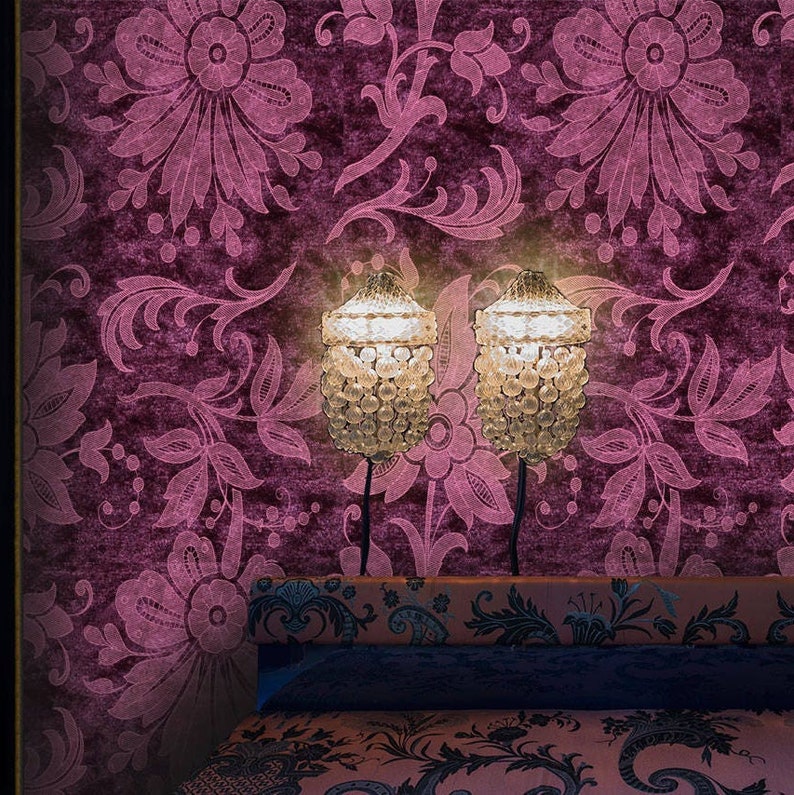 K&ouml;nnte beinhalten: Zwei Kristallperlen-Tischlampen mit warmem Schein vor dem Hintergrund einer dunkelvioletten, floral gemusterten Tapete. Die Lampen stehen auf einem dunkelvioletten Kopfteil mit gemustertem Stoff.