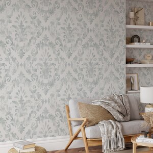 Puede incluir: Un patr&oacute;n de papel pintado damasco gris claro y blanco cubre la pared. Un sof&aacute; gris claro con estructura de madera y un coj&iacute;n tejido est&aacute; frente a la pared. Una manta gris con flecos est&aacute; sobre el sof&aacute;.