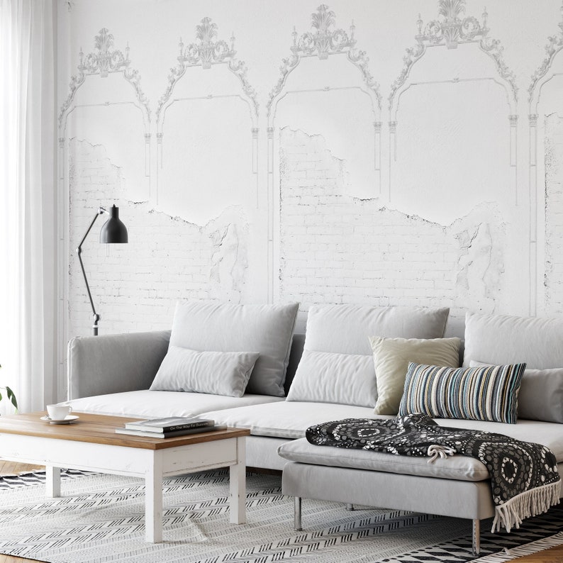 May include: A gray sectional sofa with a white distressed brick wall backdrop. The sofa has a variety of throw pillows and a black and white throw blanket. A wooden coffee table sits in front of the sofa.