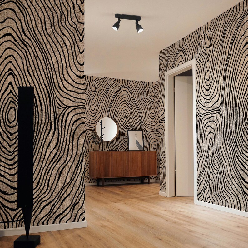 May include: An interior hallway with wood flooring and walls covered in a black and beige tree ring pattern. A wooden cabinet, round mirror, and artwork are visible. A black, modern floor lamp and ceiling lights are also present.