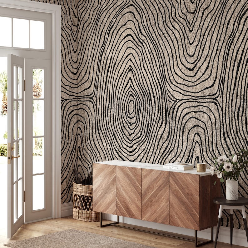 May include: A room with a beige and black tree ring patterned wallpaper. A wooden cabinet with a white marble top and a small side table are in front of the wallpaper. A door and a woven basket are also visible.