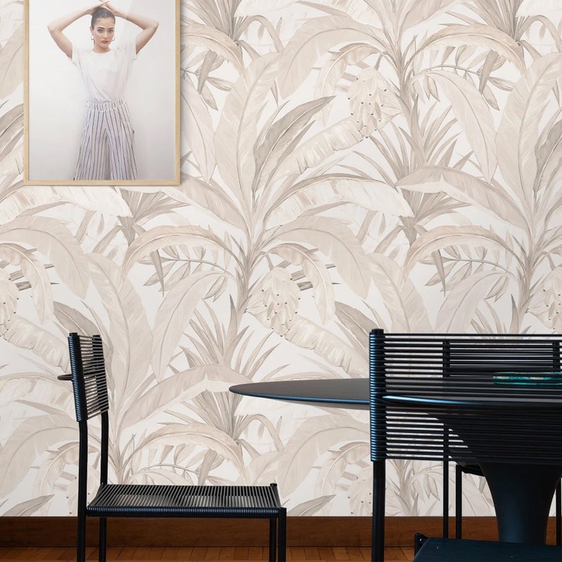 Pu&ograve; includere: Una sala da pranzo con carta da parati bianca con un motivo a foglie tropicali beige. In primo piano ci sono due sedie nere e un tavolo rotondo nero.