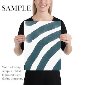 May include: A white and teal abstract art print with a series of curved lines. The print is being held by a person.