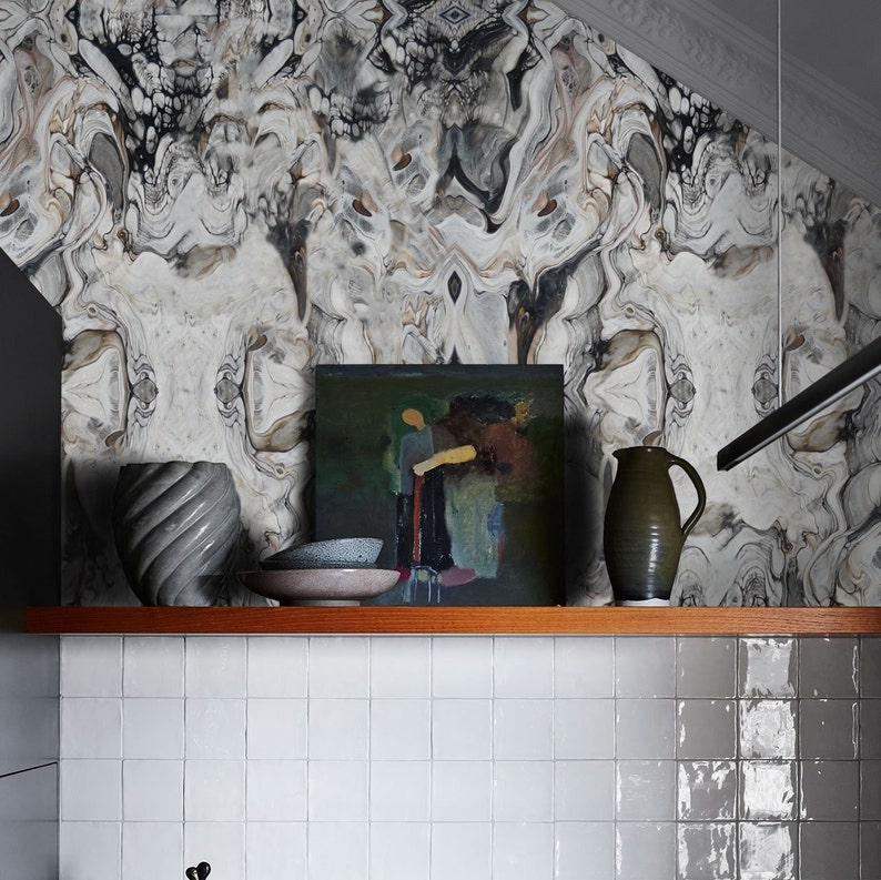 May include: A wooden shelf with a gray and brown abstract patterned wallpaper in the background. The shelf has a gray ceramic vase, a gray ceramic pitcher, a gray ceramic bowl, and a framed painting of a person in a green field.