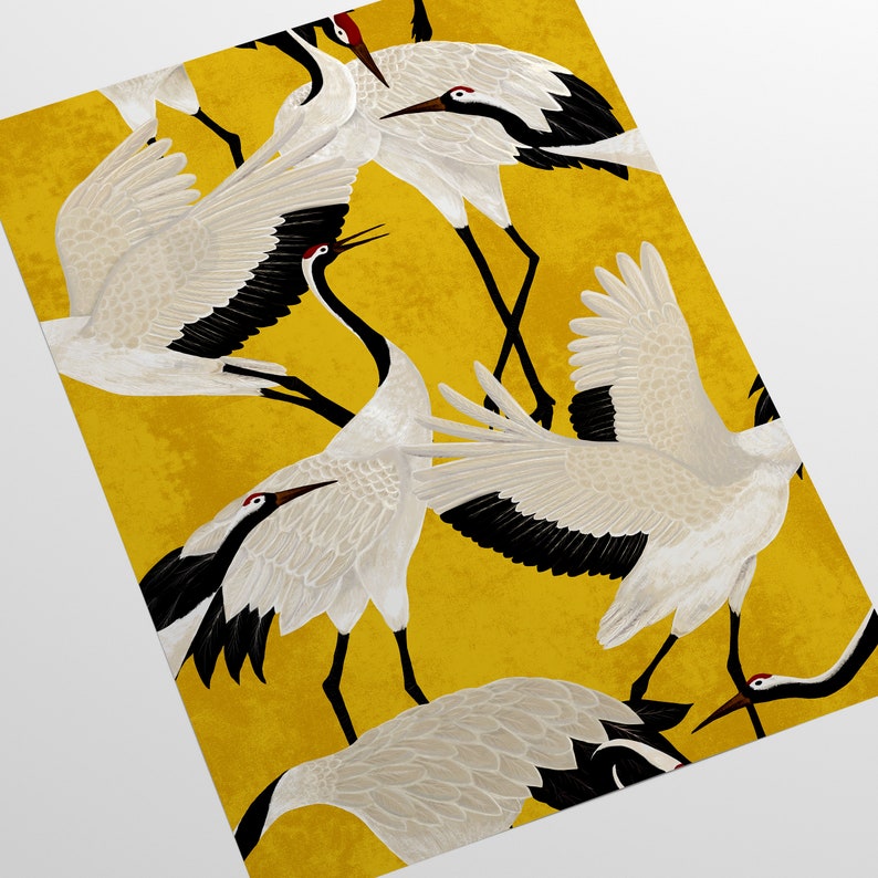 May include: A decorative print featuring a pattern of white cranes with black wingtips and red accents against a textured yellow background. The cranes are depicted in various poses, some with wings spread, creating a dynamic and artistic design.
