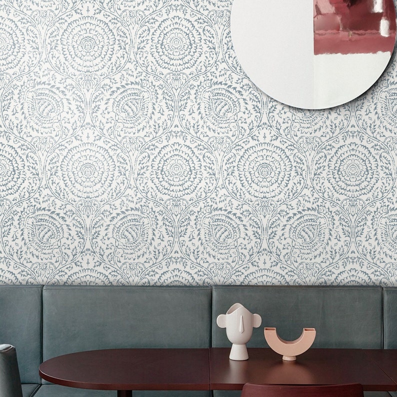 May include: A white wall with a blue and white patterned wallpaper. The wallpaper features a repeating design of stylized flowers and leaves. A gray couch is in front of the wall, and a wooden table with two decorative objects is in front of the couch.
