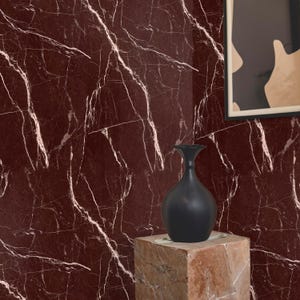 Può includere: Un vaso in ceramica nero si trova su un piedistallo quadrato di colore marrone chiaro su uno sfondo di carta da parati in marmo rosso con venature bianche.