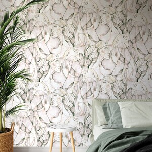 Puede incluir: Un papel tapiz blanco con un patr&oacute;n repetitivo de caras abstractas en tonos de rosa, verde y marr&oacute;n. El papel tapiz se muestra en un ambiente de dormitorio con una cama y una mesa peque&ntilde;a.