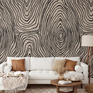 May include: A living room scene featuring a white sectional sofa with brown and beige throw pillows. The wall behind the sofa is covered in a beige and black tree ring pattern wallpaper. A wooden coffee table and floor lamp complete the decor.
