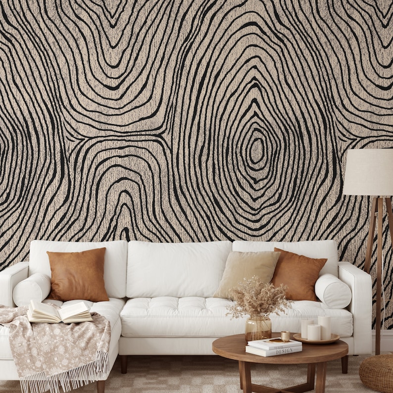 May include: A living room scene featuring a white sectional sofa with brown and beige throw pillows. The wall behind the sofa is covered in a beige and black tree ring pattern wallpaper. A wooden coffee table and floor lamp complete the decor.