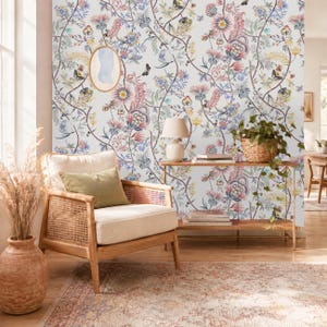 Può includere: Carta da parati con un motivo ripetitivo di colorate illustrazioni botaniche, tra cui fiori rosa, blu e gialli, foglie verdi e piccole farfalle su sfondo bianco, applicata su una parete dietro una sedia e un tavolo in legno.