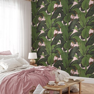 May include: A pink bedroom with a bed with a pink blanket and white pillows. The wall behind the bed is covered in a wallpaper with a large-scale banana leaf pattern in shades of green on a pink background.