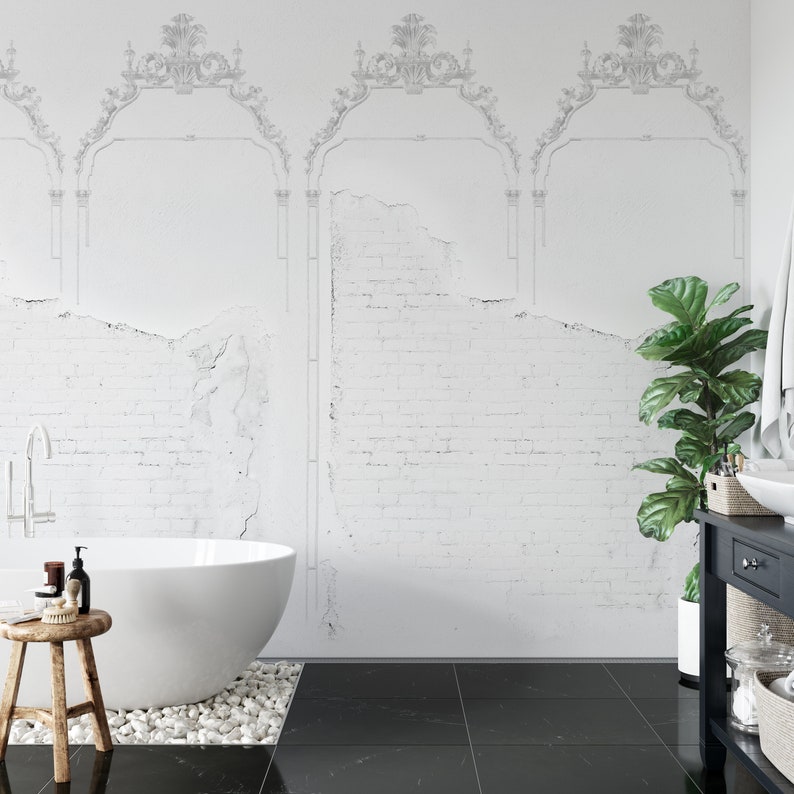 May include: A white freestanding bathtub with a white tiled wall behind it. The wall has a distressed brick pattern and a decorative molding design. A black tiled floor is in the foreground. A green plant is in a white pot on the right side of the image.