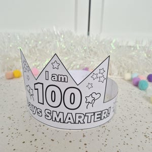 May include: A white paper crown with the text "I am 100 days SMARTER!" in black. The crown has star and heart decorations. Perfect for a child's 100th day of school celebration.