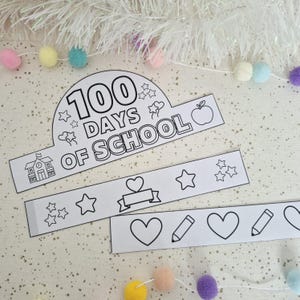May include: Black and white paper crown and bands with the text "100 Days of School". The crown features stars, an apple, and a schoolhouse. The bands have hearts, stars, and pencils. Decorative pom-poms are in the background.