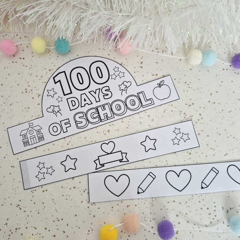 May include: Black and white paper crown and bands with the text "100 Days of School". The crown features stars, an apple, and a schoolhouse. The bands have hearts, stars, and pencils. Decorative pom-poms are in the background.